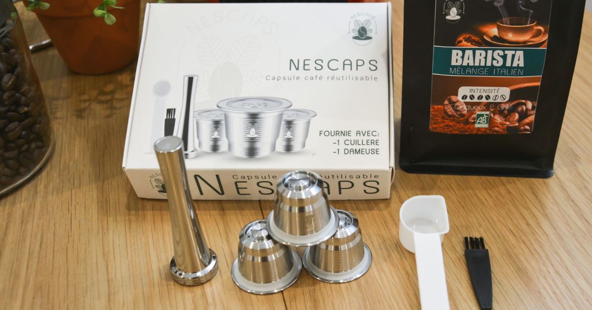 Capsule réutilisable Nescaps, dameuse et café en grain présentés sur une table en bois